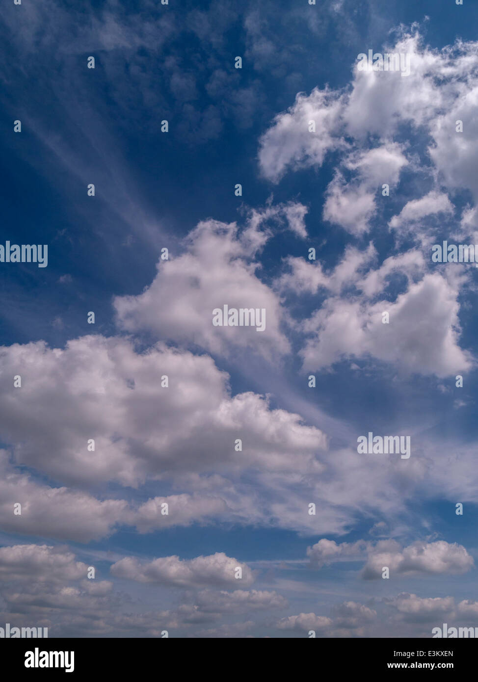 White cumulus clouds against deep blue sky with wispy high level cirrus clouds Stock Photo