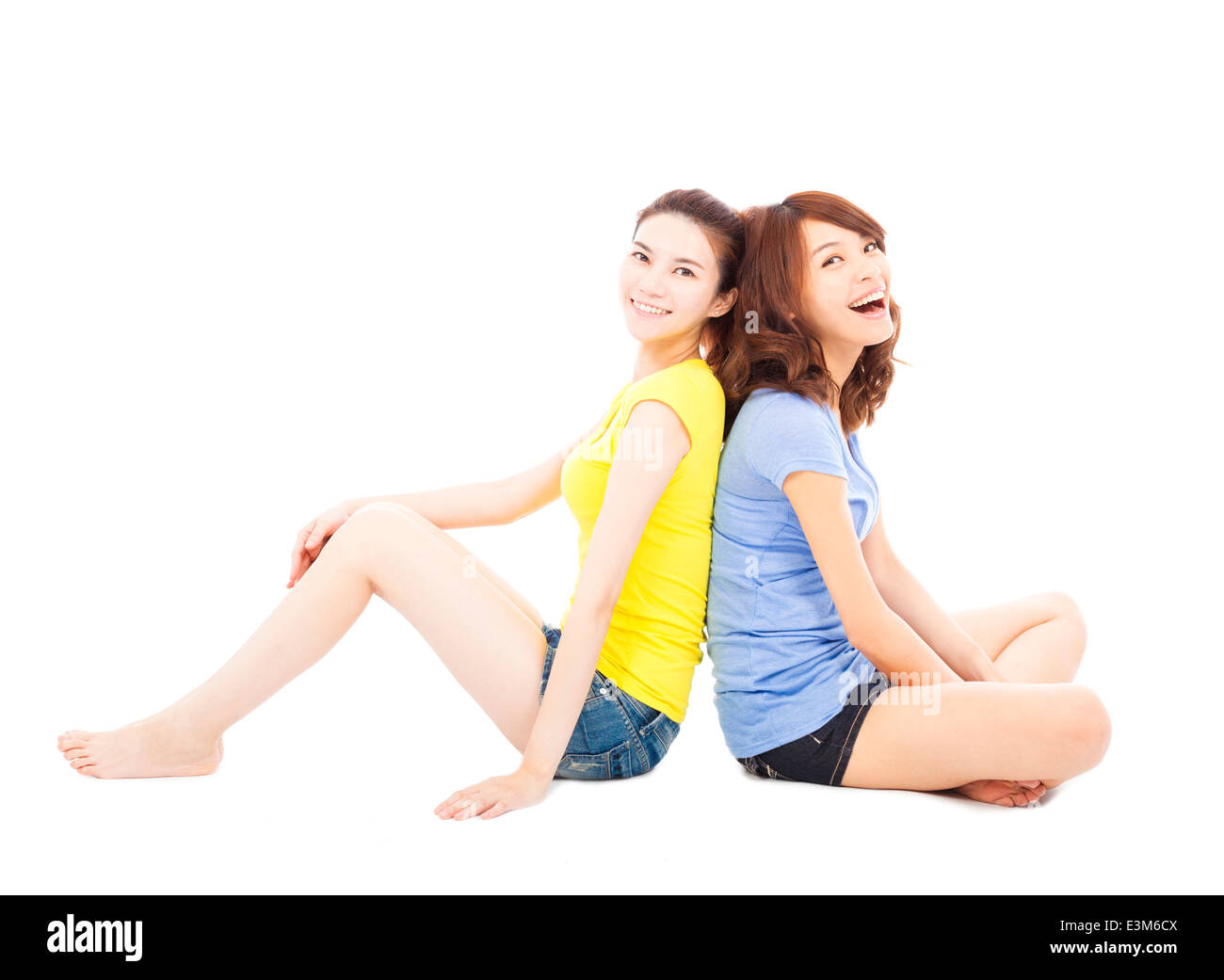 two smiling young woman sitting and back to back Stock Photo