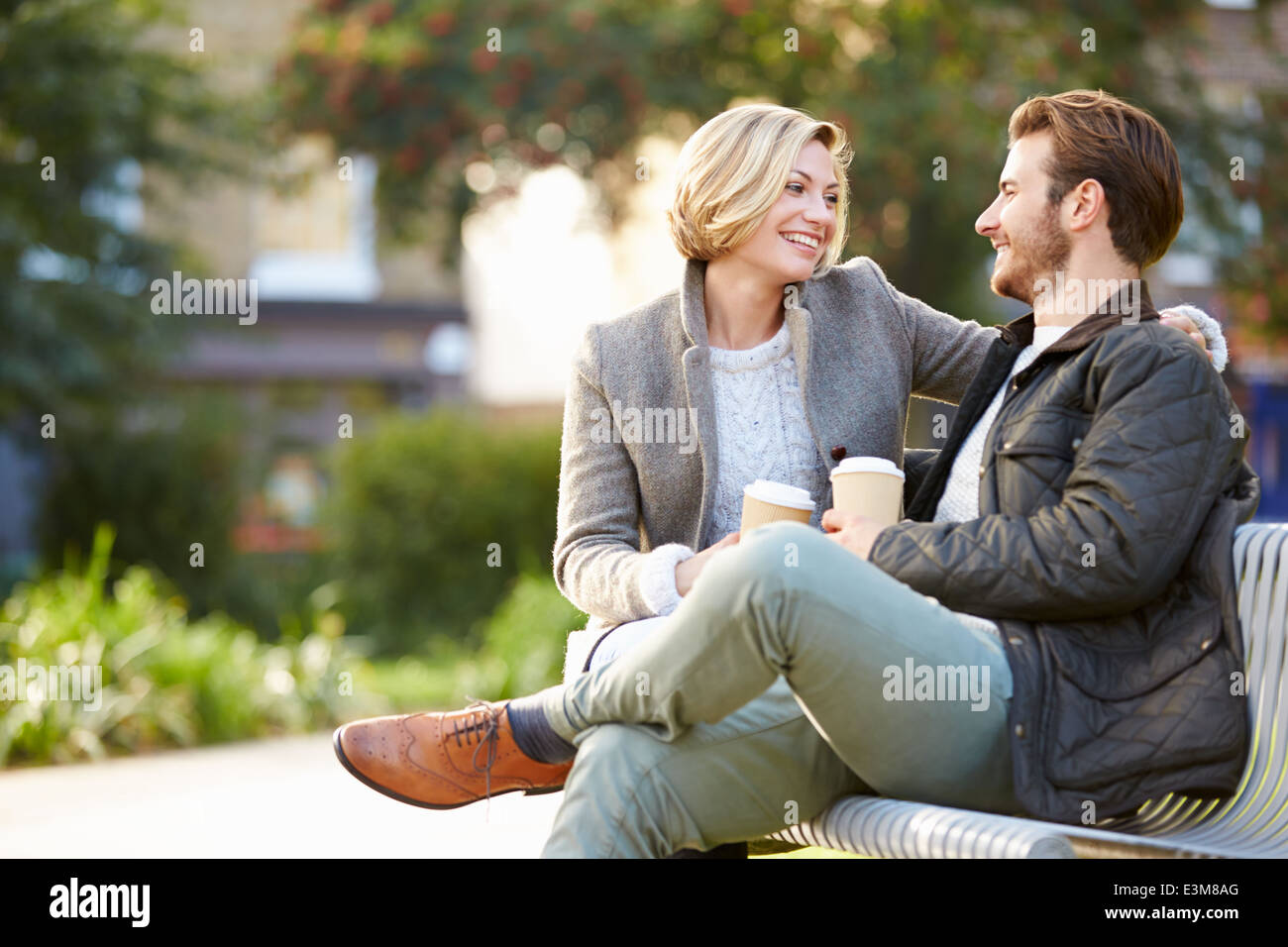 Couple Relaxing On Park Bench With Takeaway Coffee Stock Photo - Alamy