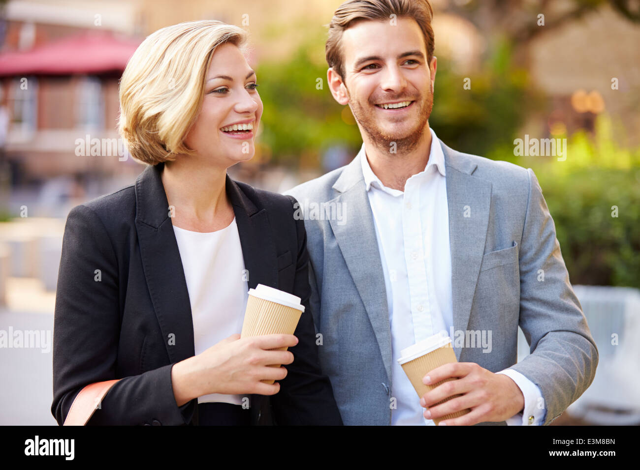 Business Couple Walking Through Park With Takeaway Coffee Stock Photo