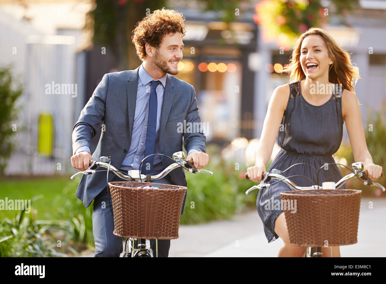 Businesswoman And Businessman Riding Bike Through City Park Stock Photo