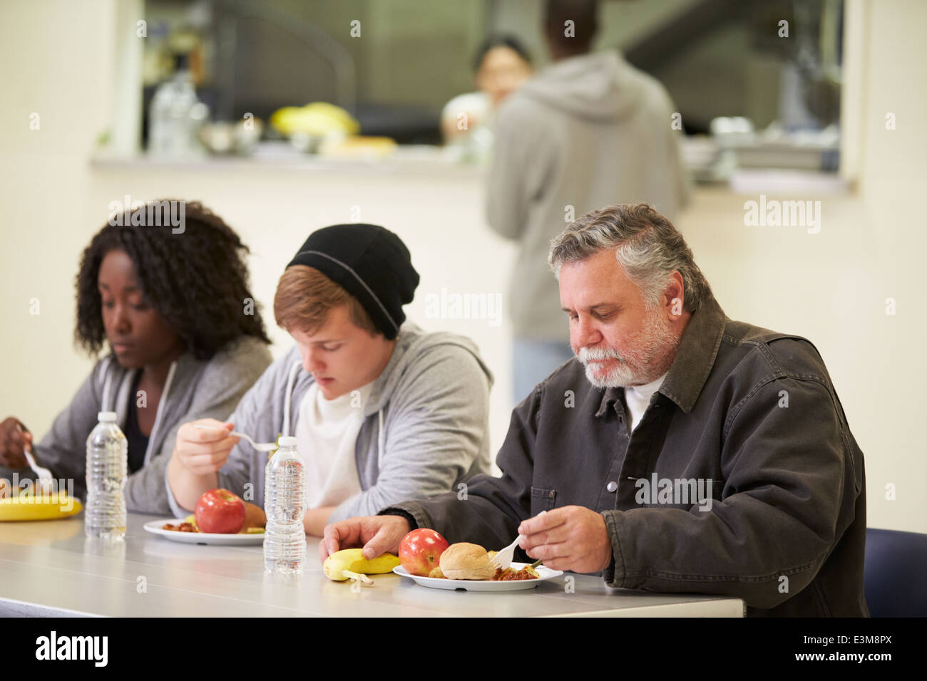 People Sitting At Table Eating Food In Homeless Shelter Stock Photo