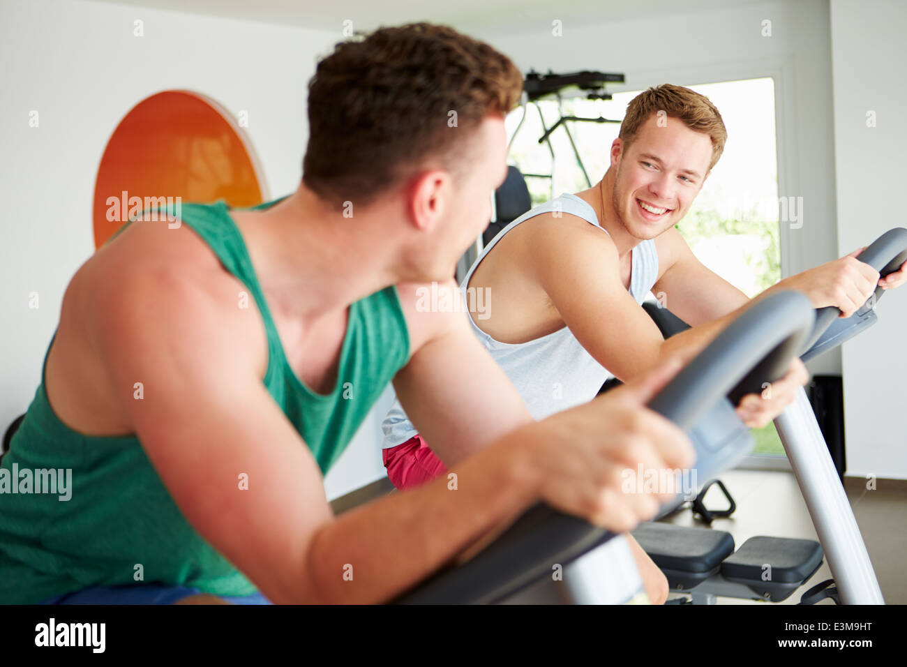 Two Young Men Training In Gym On Cycling Machines Together Stock Photo