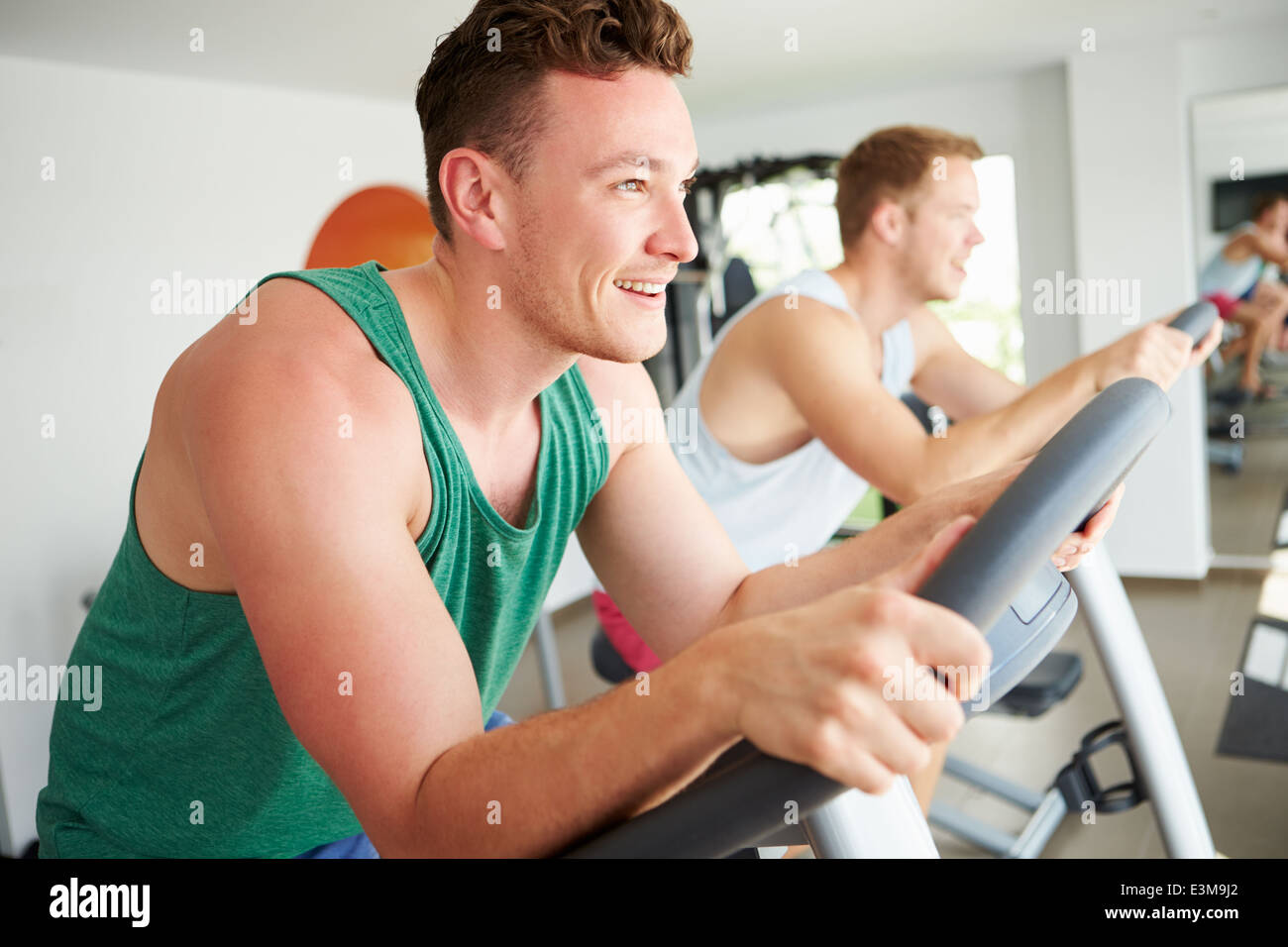 Two Young Men Training In Gym On Cycling Machines Together Stock Photo