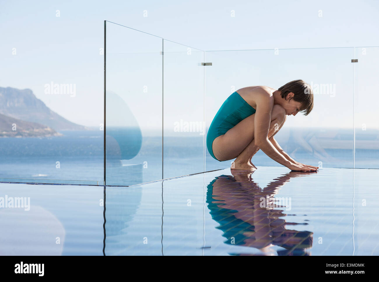 Woman crouching over infinity pool with ocean view Stock Photo
