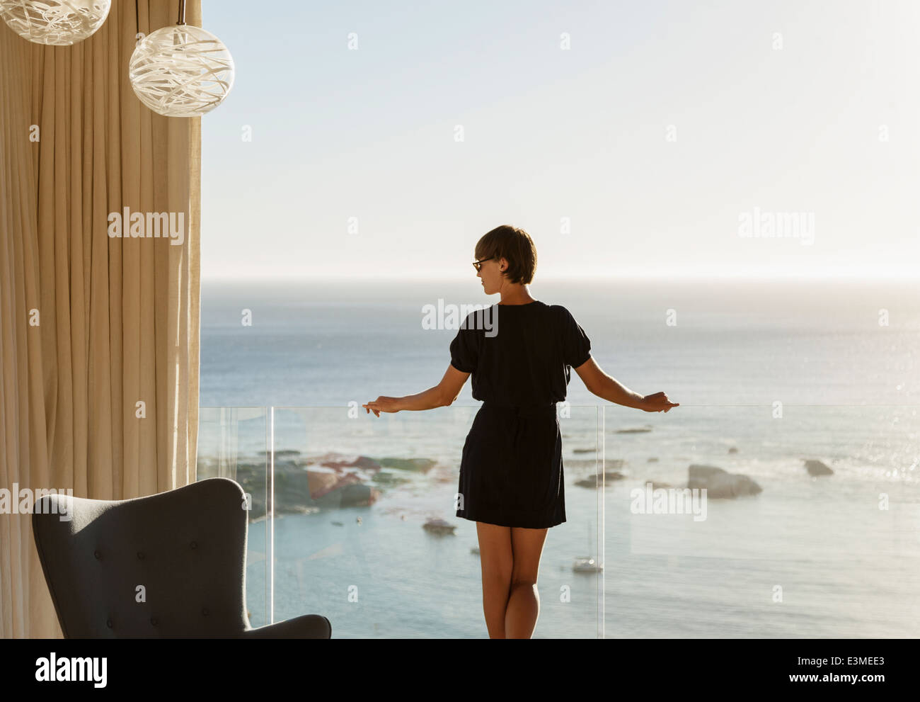 Woman standing at balcony railing overlooking ocean Stock Photo