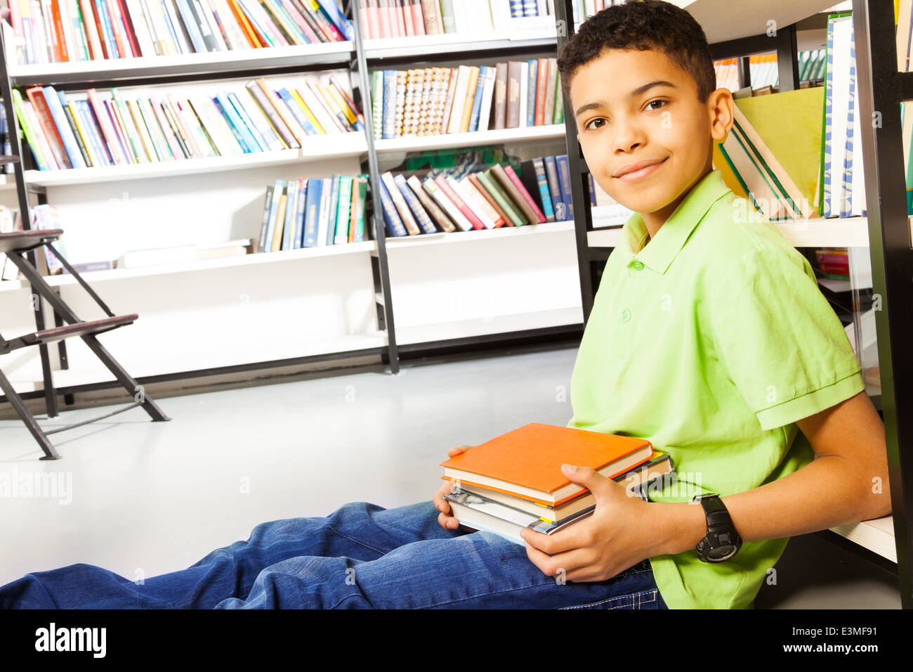Pupil with pile of books sits on floor in library Stock Photo - Alamy