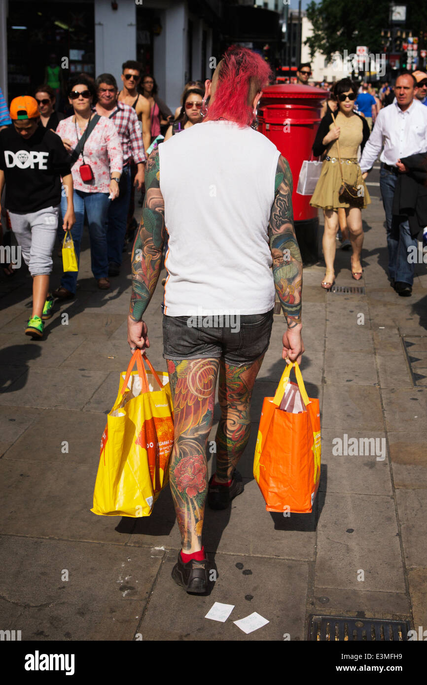 Shopper / consumer: Man with red hair, tattooed arms and legs, carrying shopping bags, central London, UK Stock Photo