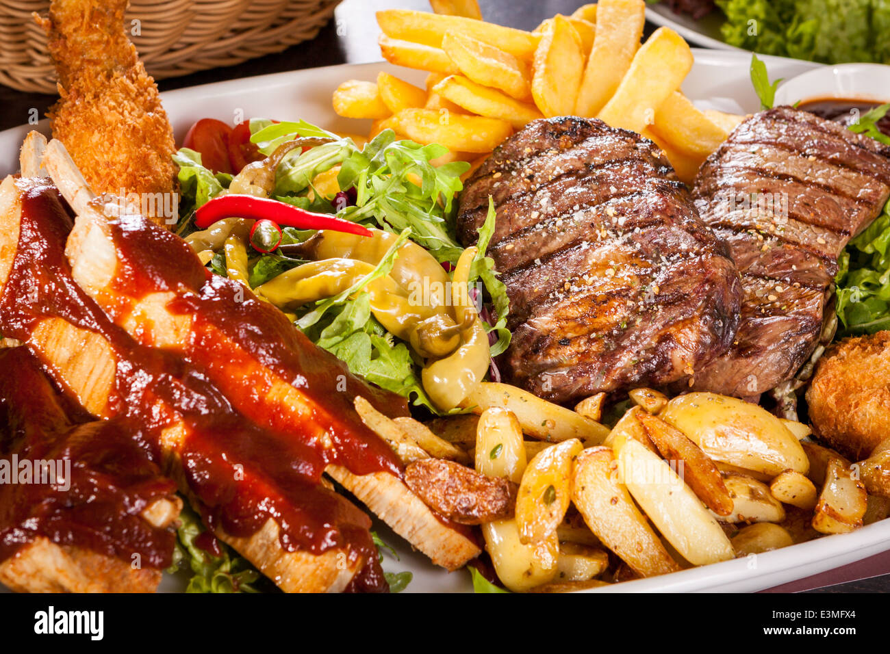 Wholesome platter of mixed meats including grilled steak, crispy crumbed chicken and beef on a bed of fresh leafy green mixed salad served with French fries and chutney or BBQ sauce in a dish Stock Photo