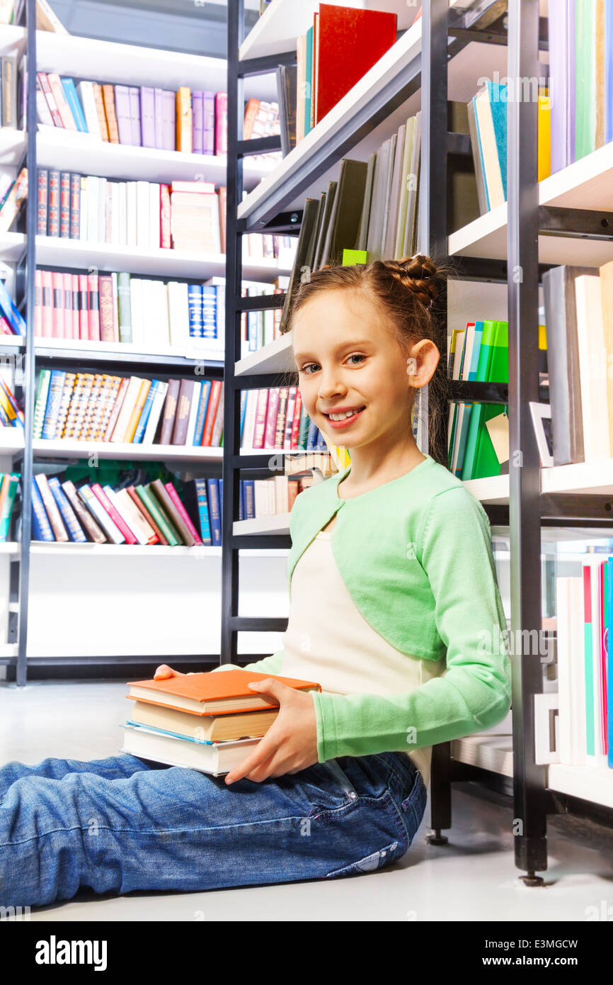 Happy girl with books sits on floor in library Stock Photo - Alamy