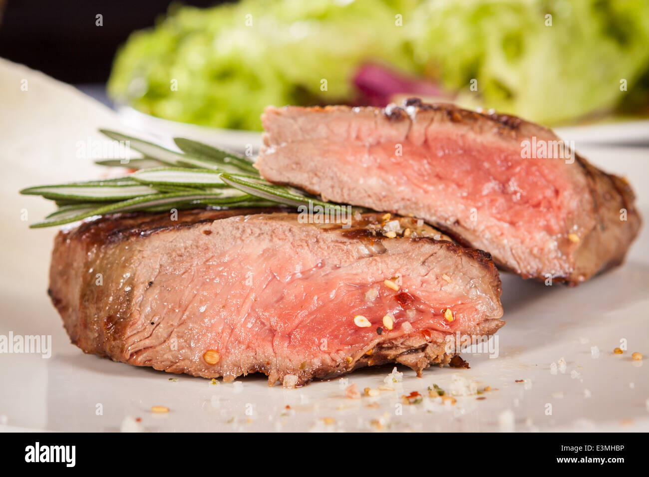 Succulent medium rare beef steak sliced through to display the tender red flesh and seasoned with spices and fresh rosemary, clo Stock Photo