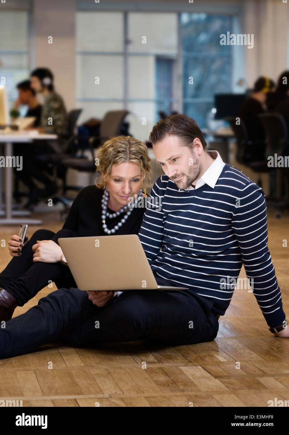 Smartly dressed business people using laptop while sitting on floor at office Stock Photo