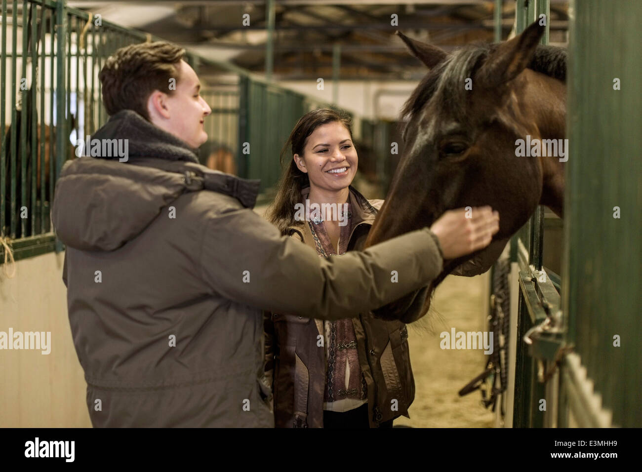 Happy young couple stroking horse in stable Stock Photo