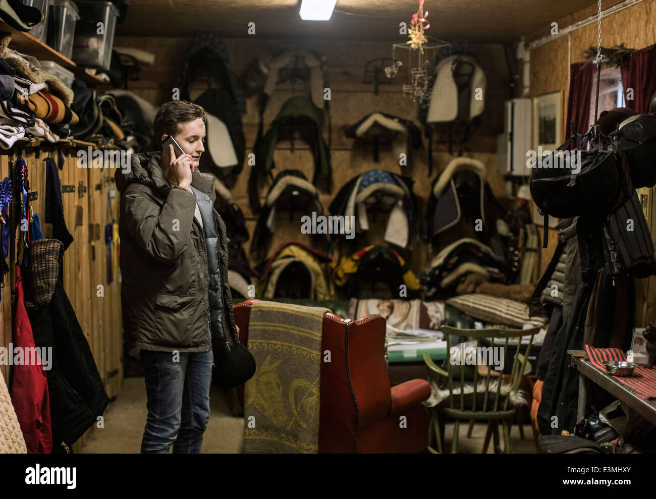 Young man answering smart phone in horse stable Stock Photo