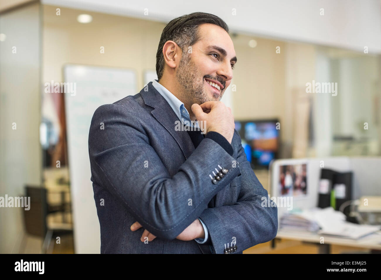 Smiling mid adult businessman with hand on chin looking away in office Stock Photo