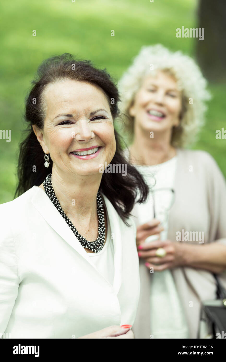 Portrait of happy senior woman at park with friend standing in ...