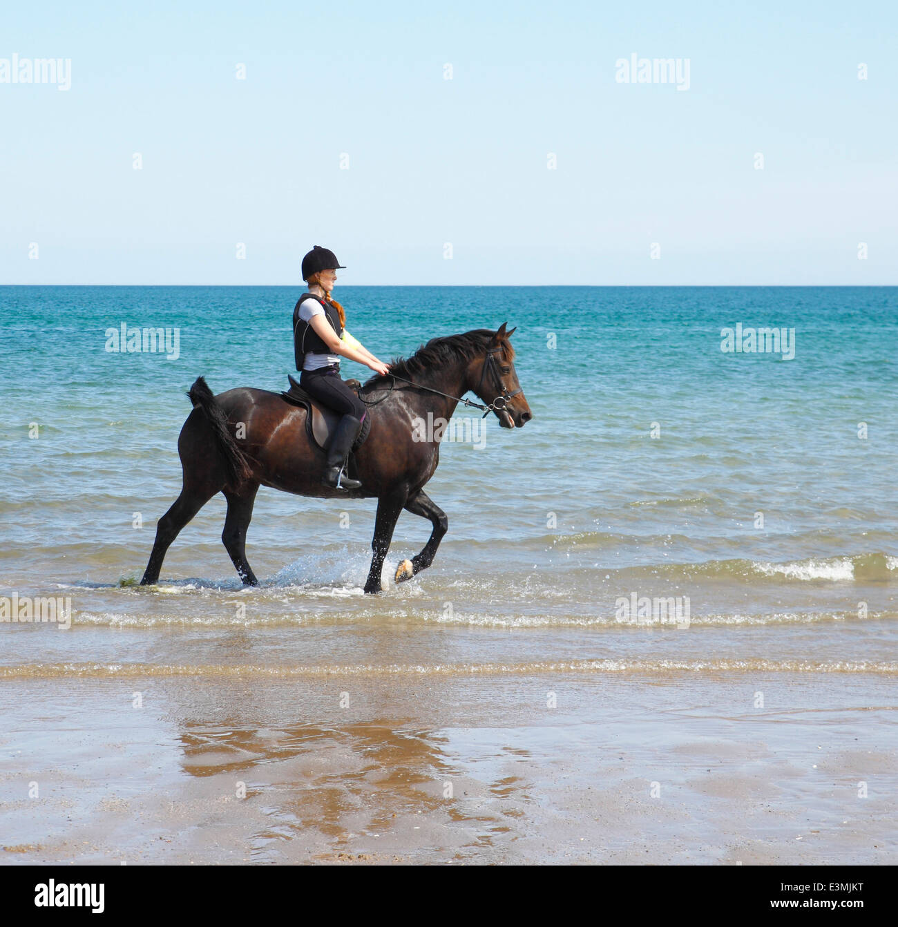 Young woman riding her horse in the sea. Stock Photo