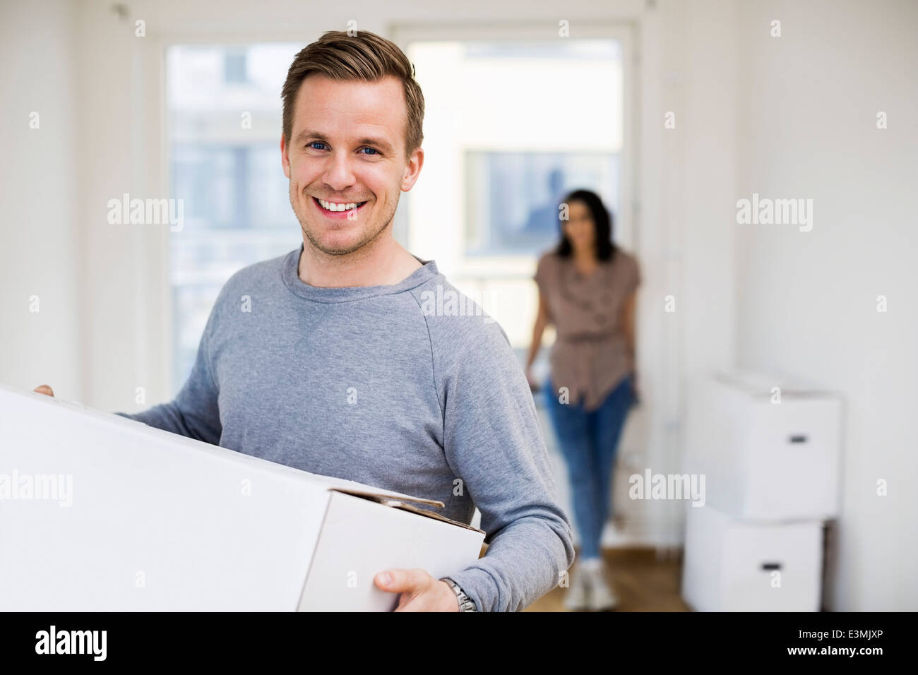 Portrait of happy man carrying moving box with woman in background at ...