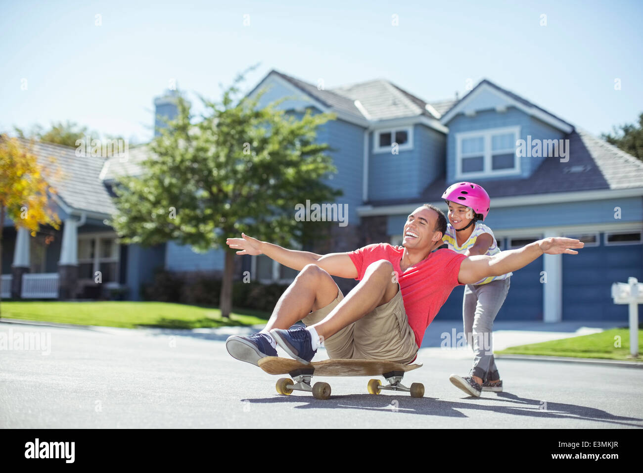 Daughter pushing father on skateboard Stock Photo