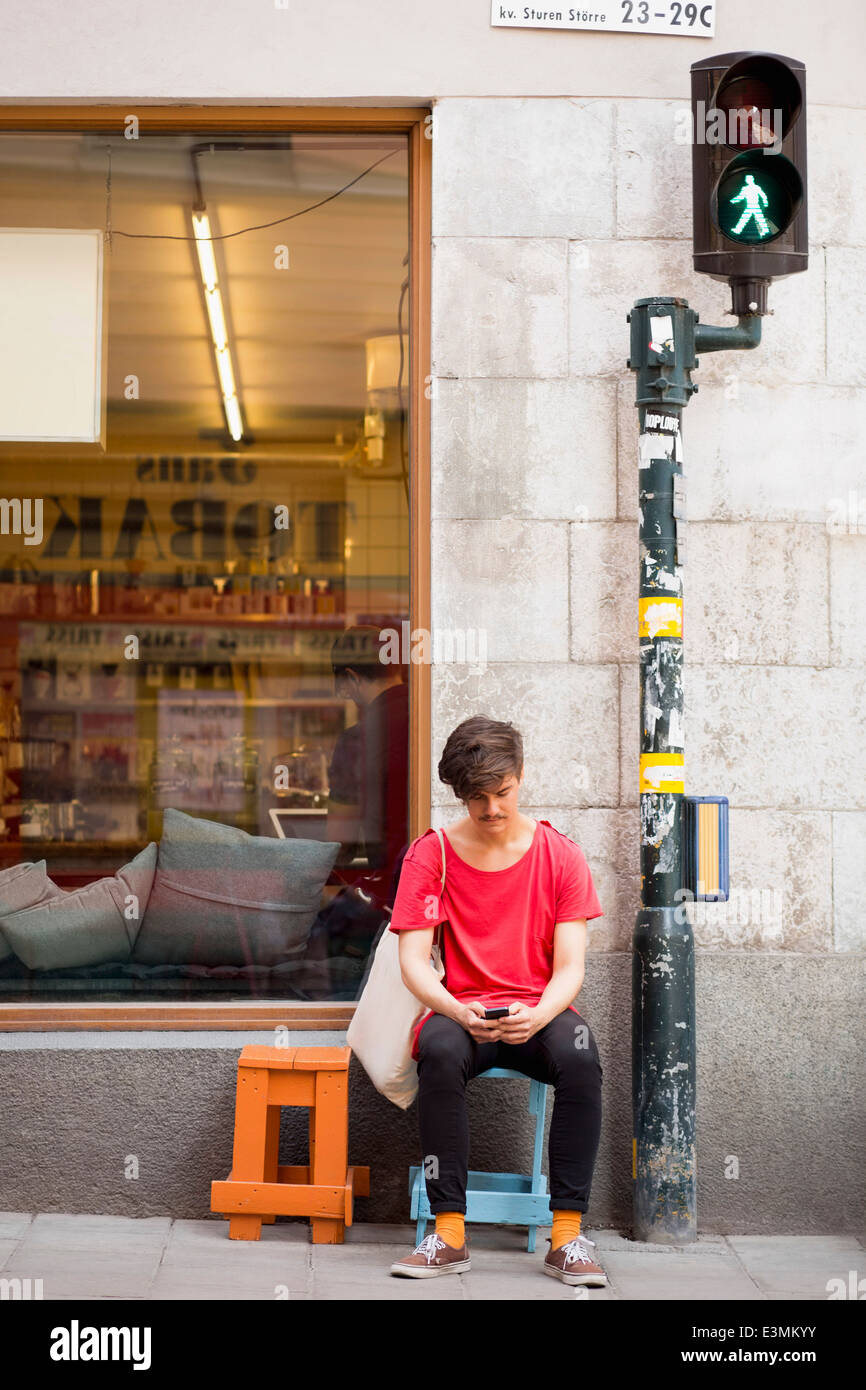 Full length of young man reading text message on mobile phone at sidewalk Stock Photo