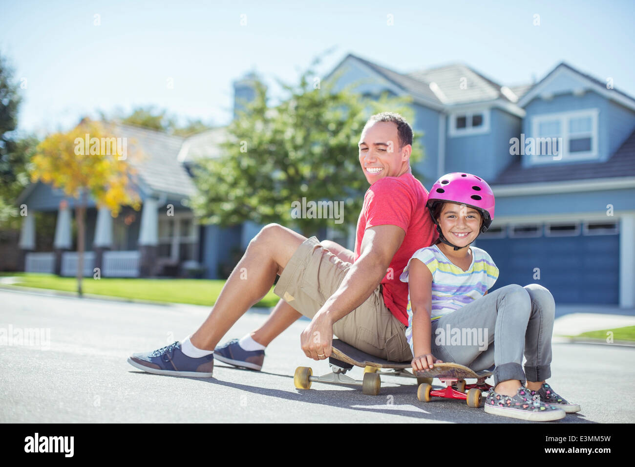 Father and daughter sitting on skateboard Stock Photo