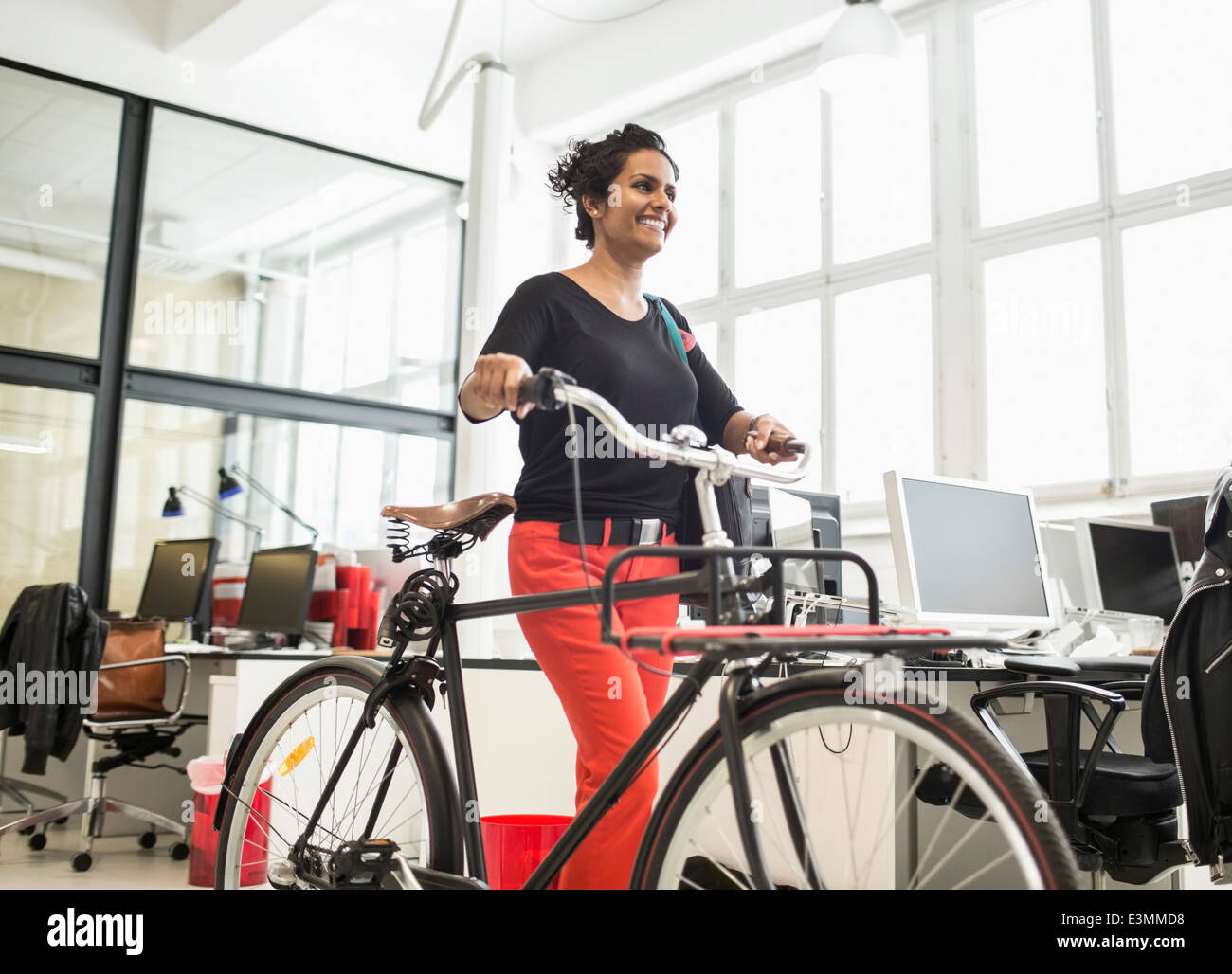 Smiling businesswoman with bicycle walking in creative office Stock Photo