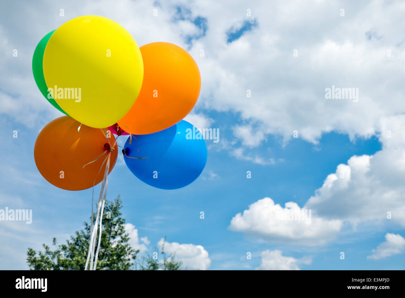 Colorful helium filled party balloons floating, tethered against a sunny summer sky Stock Photo