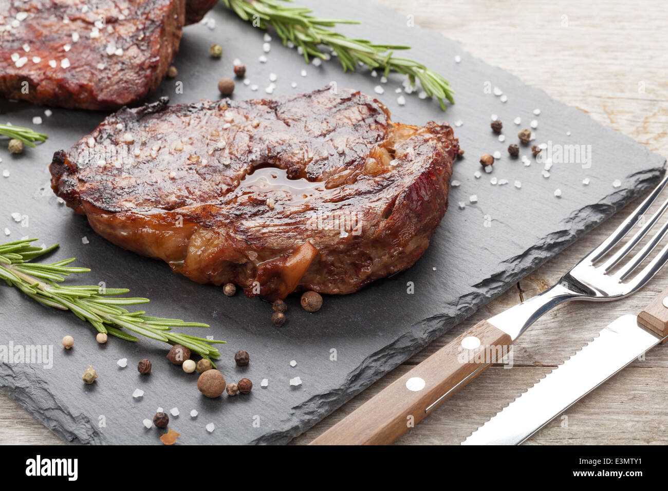 Beef steaks with rosemary and spices on wooden table Stock Photo