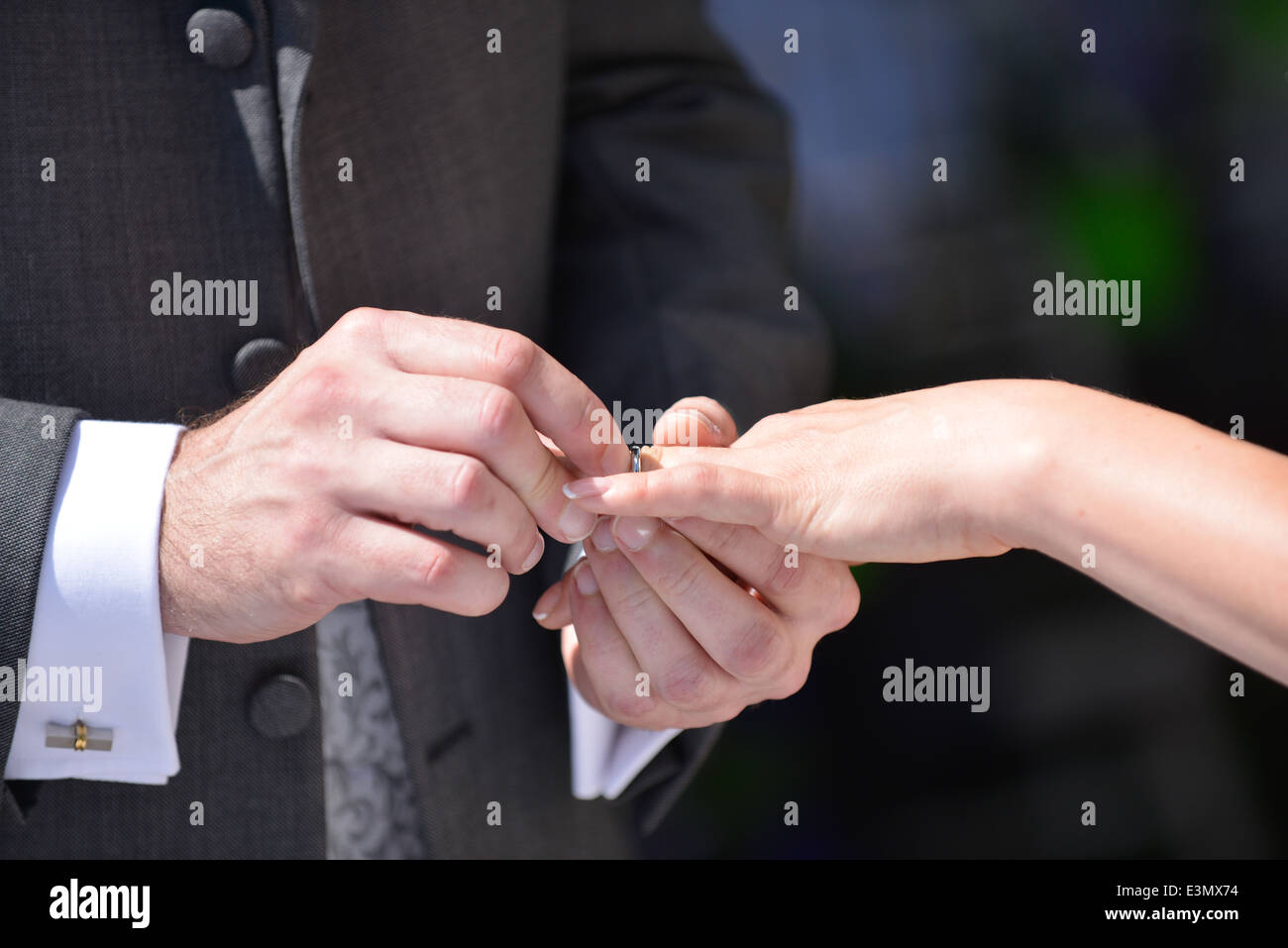 A groom holds his wifes hand as he places a wedding ring on his brides finger during a traditional wedding ceremony Stock Photo