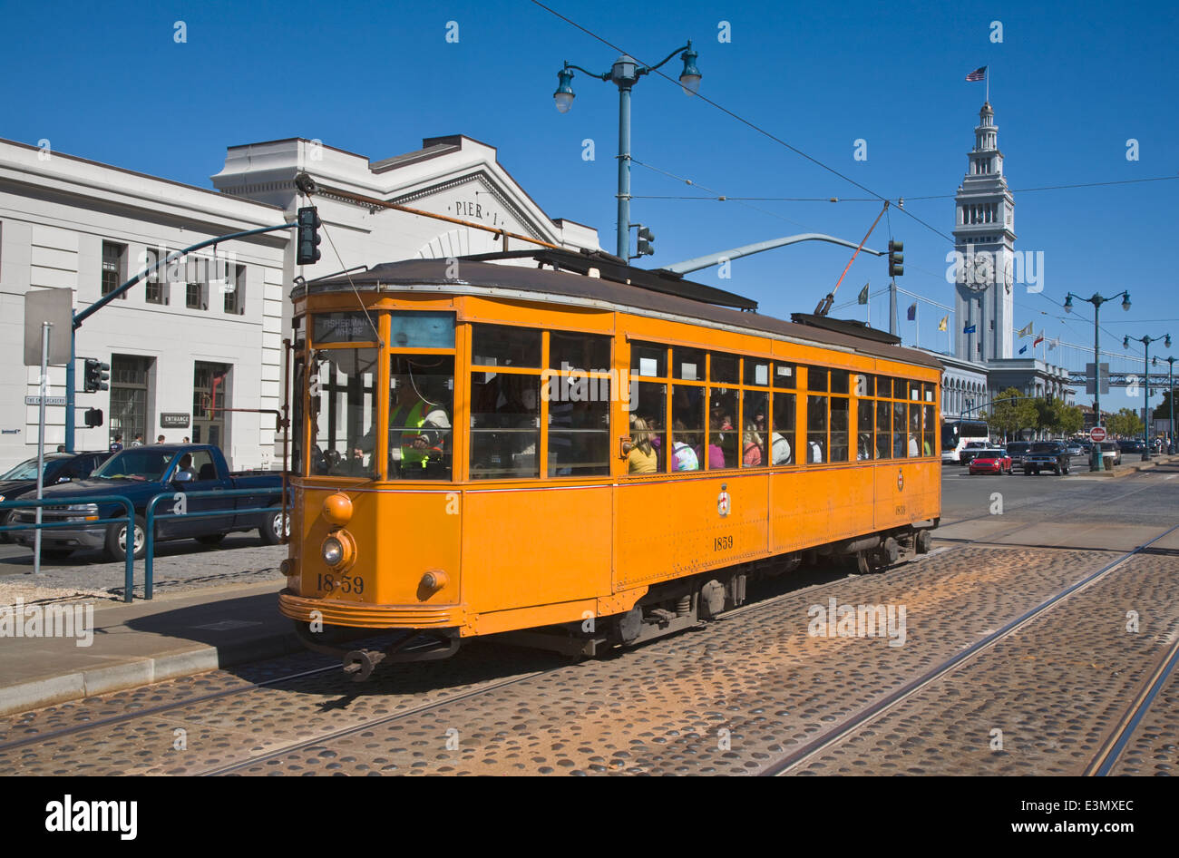 A historical CABLE CAR runs along the tracks in front of PIER 3 and the FERRY BUILDING on THE EMBARCADERO - SAN FRANCISCO, CALIF Stock Photo