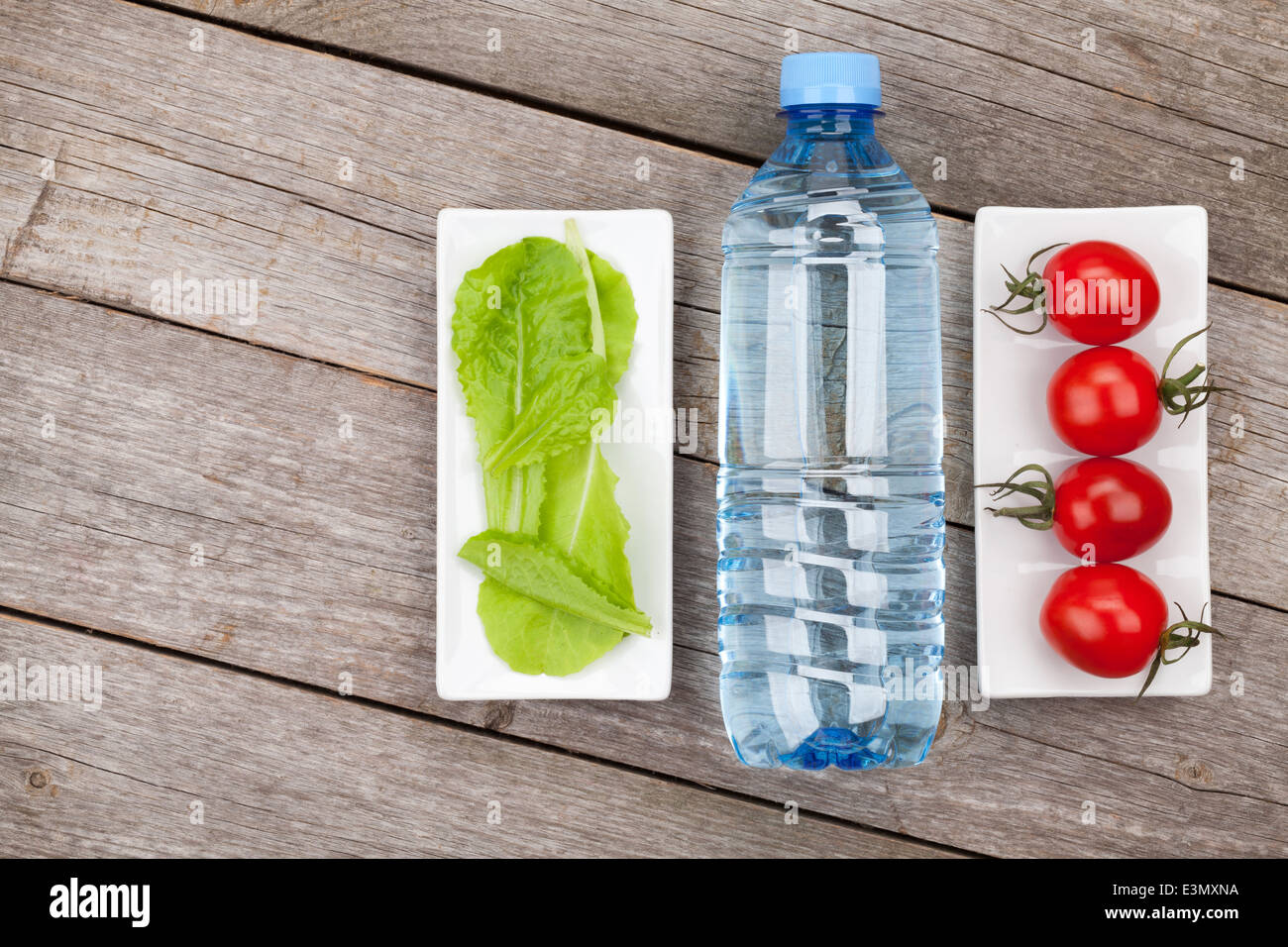 Green salad leaves, water bottle and tomatoes. Healthy food on wooden table background with copy space Stock Photo
