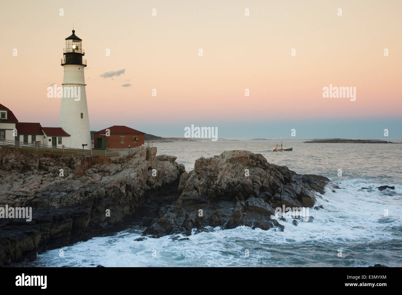Summer sun sets as Portland Head lighthouse guides fishing boat out of Portland's Harbor. Stock Photo