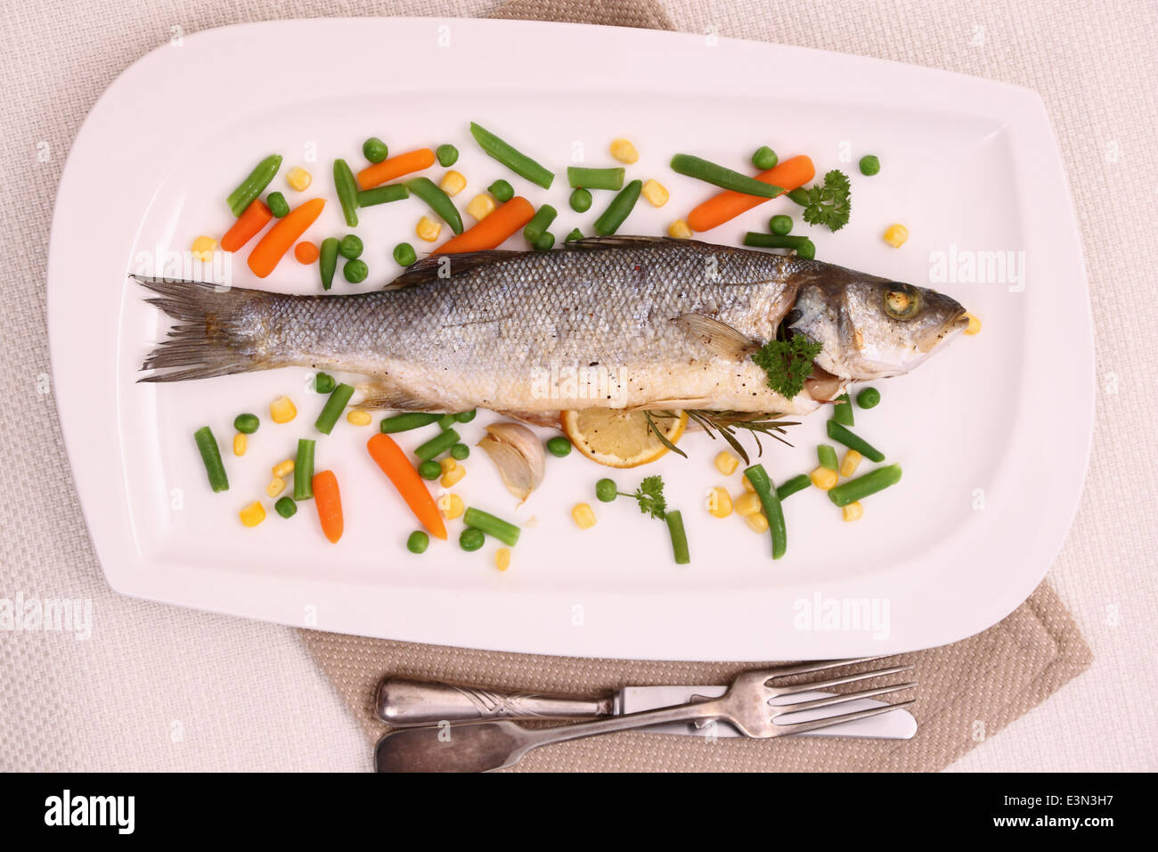 Fried whole sea bass with vegetables and lemon, close up Stock Photo