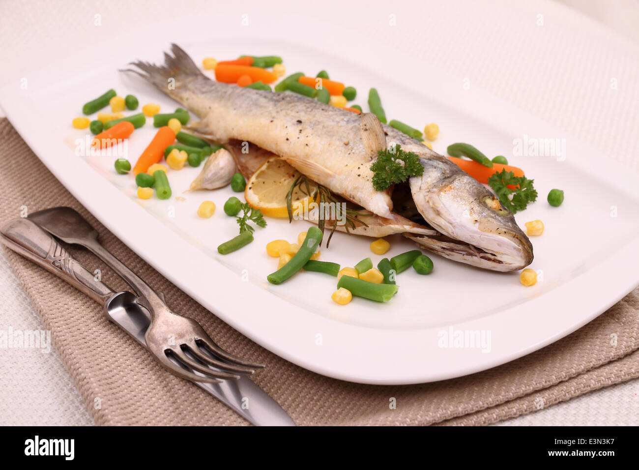 Fried whole sea bass, vegetables and lemon, close up Stock Photo