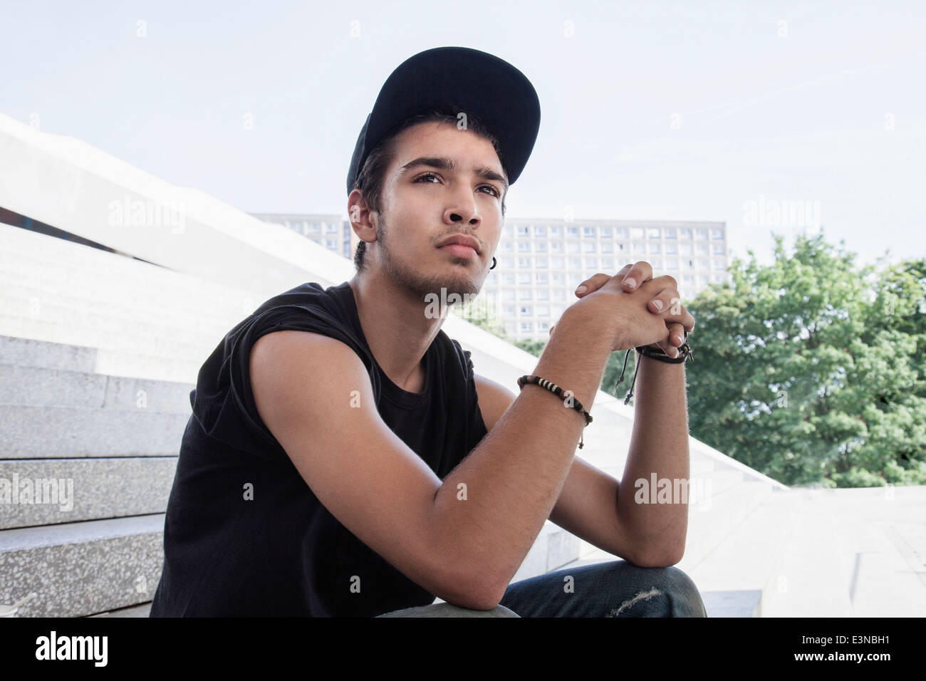 Thoughtful young man with hands clasped sitting on steps outdoors Stock Photo