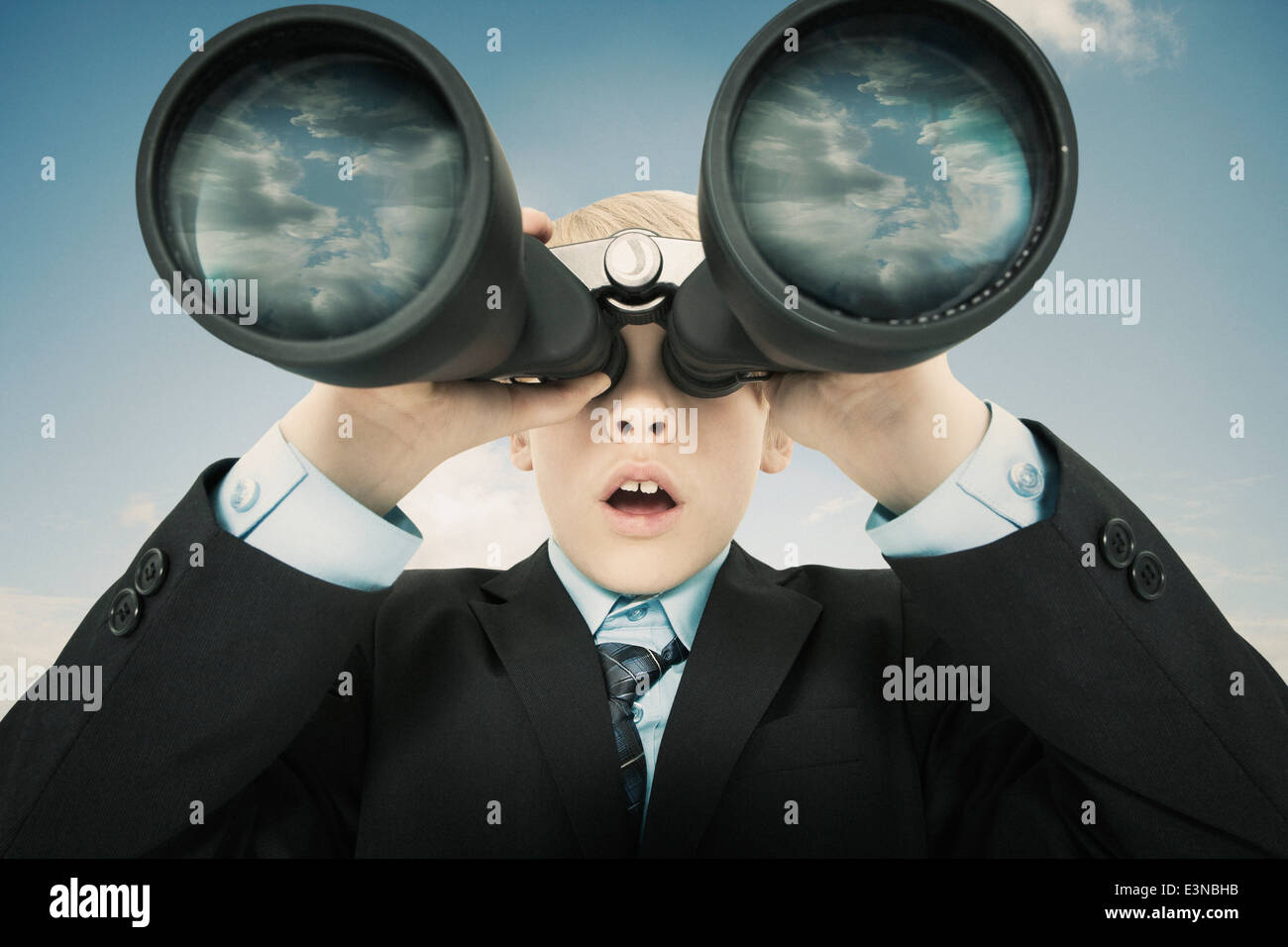 Boy dressed as businessman looking through binoculars against sky Stock Photo