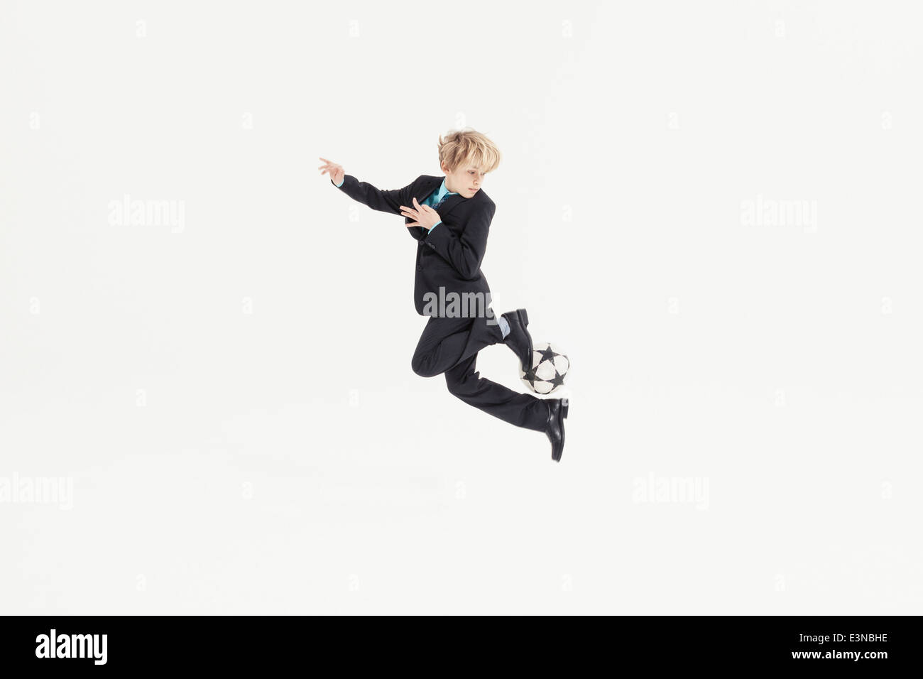 Full length of boy dressed as businessman playing soccer against white background Stock Photo