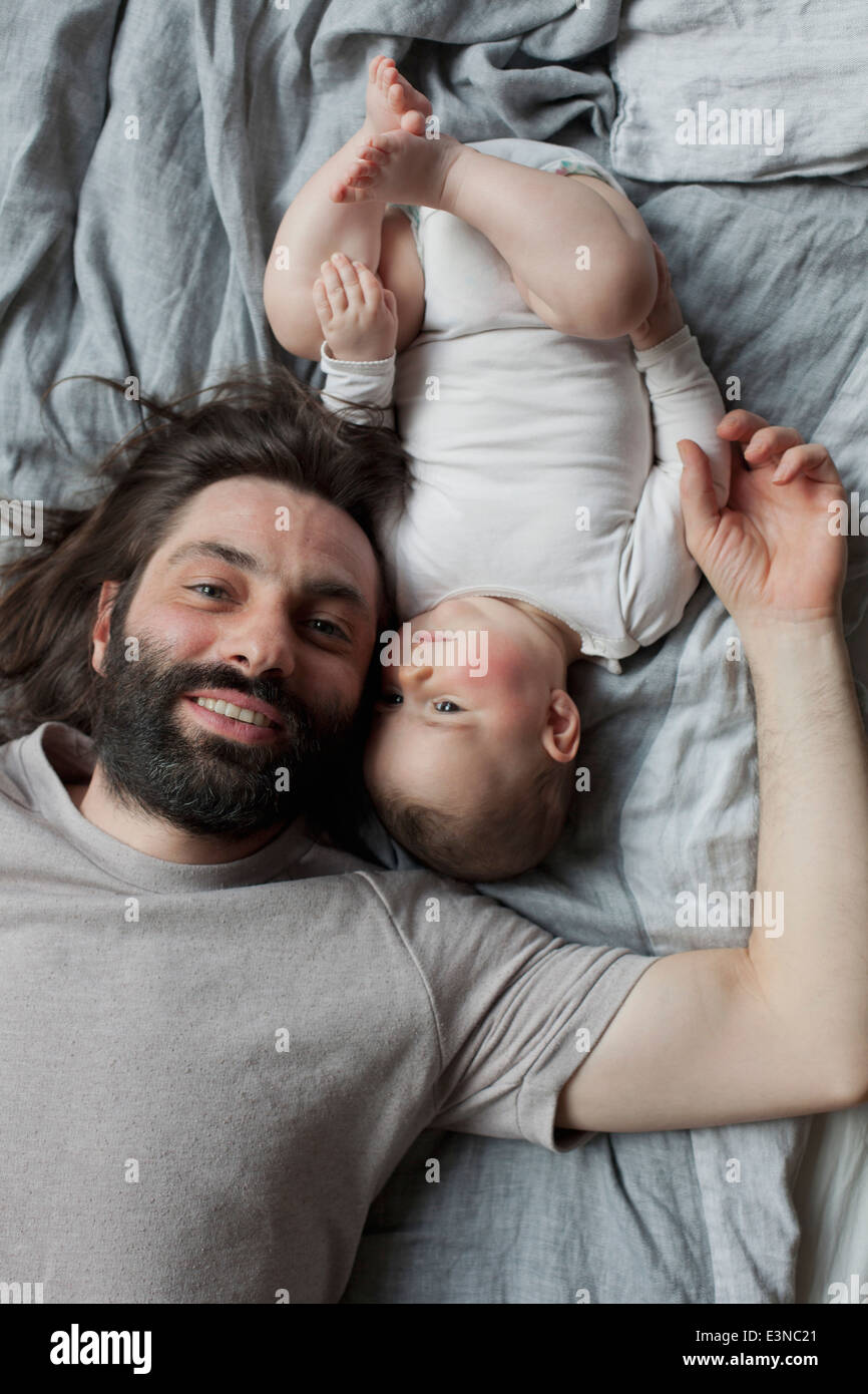 Portrait of smiling father with baby girl lying in bed Stock Photo
