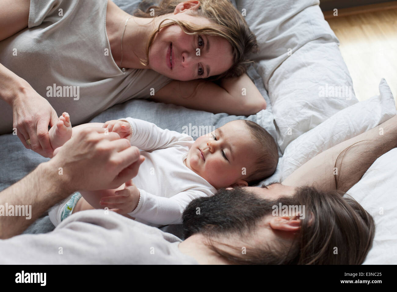 Affectionate parents looking at baby girl while relaxing on mattress Stock Photo