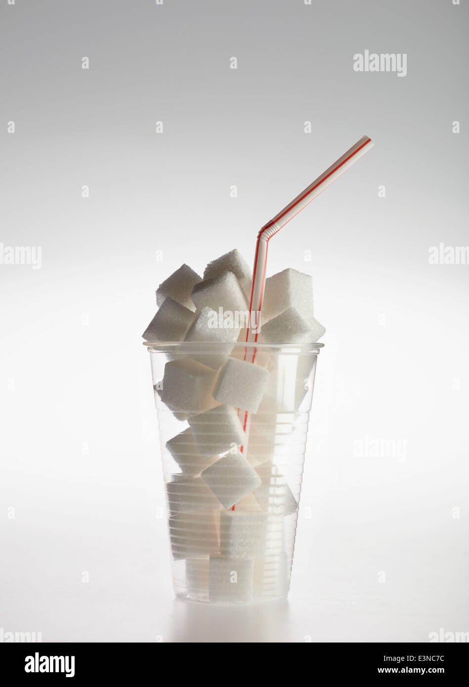 Straw in plastic glass filled with sugar cubes over gray background Stock Photo