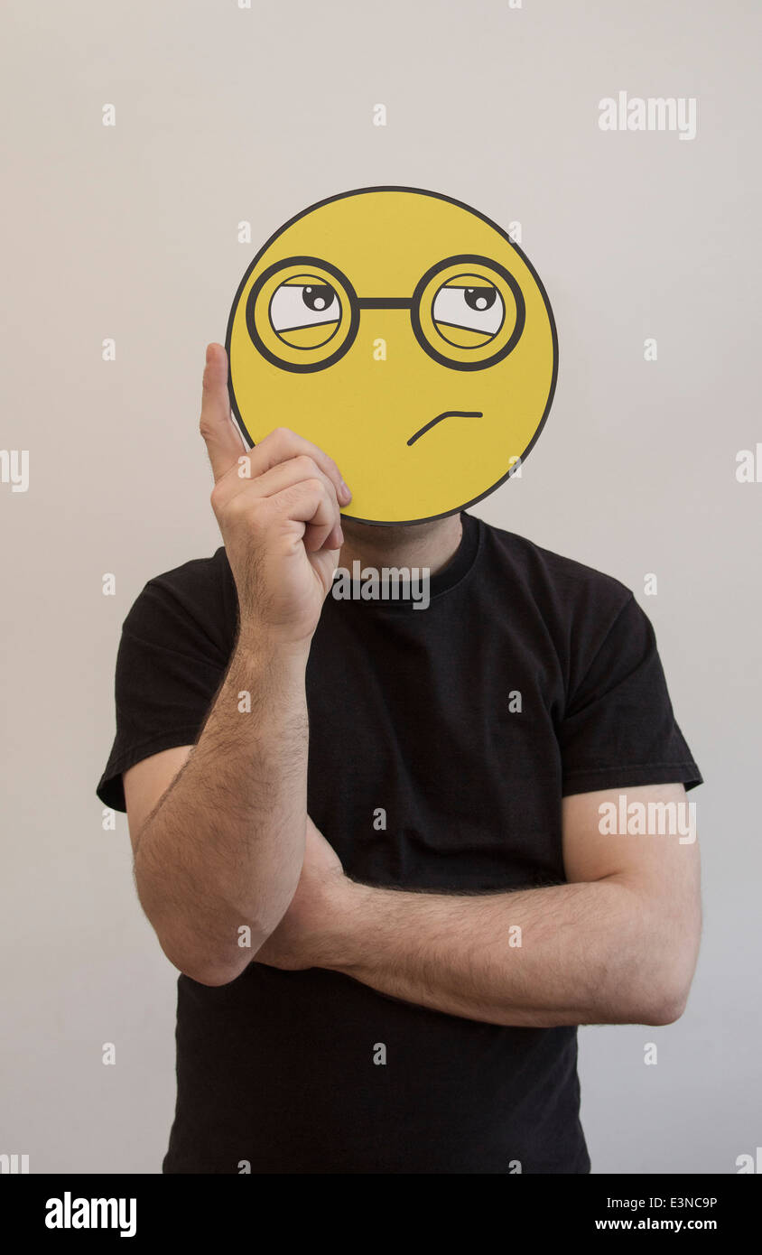 Man holding a confused emoticon face in front of his face Stock Photo