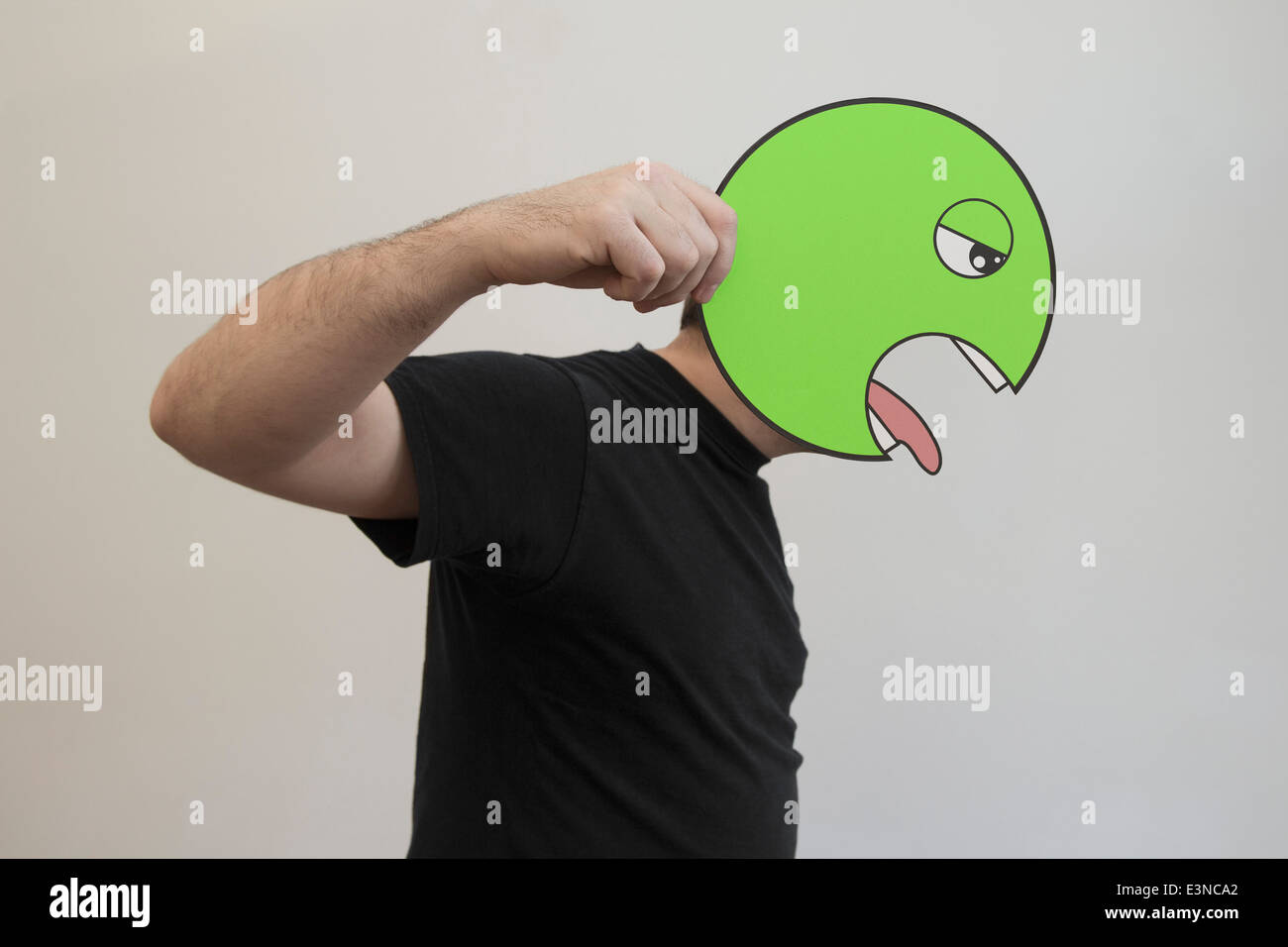 Side view of man holding a green vomit emoticon face in front of his face Stock Photo