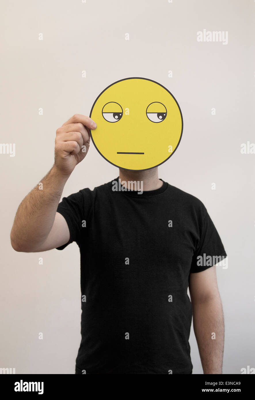 Man holding a bored emoticon face in front of his face Stock Photo