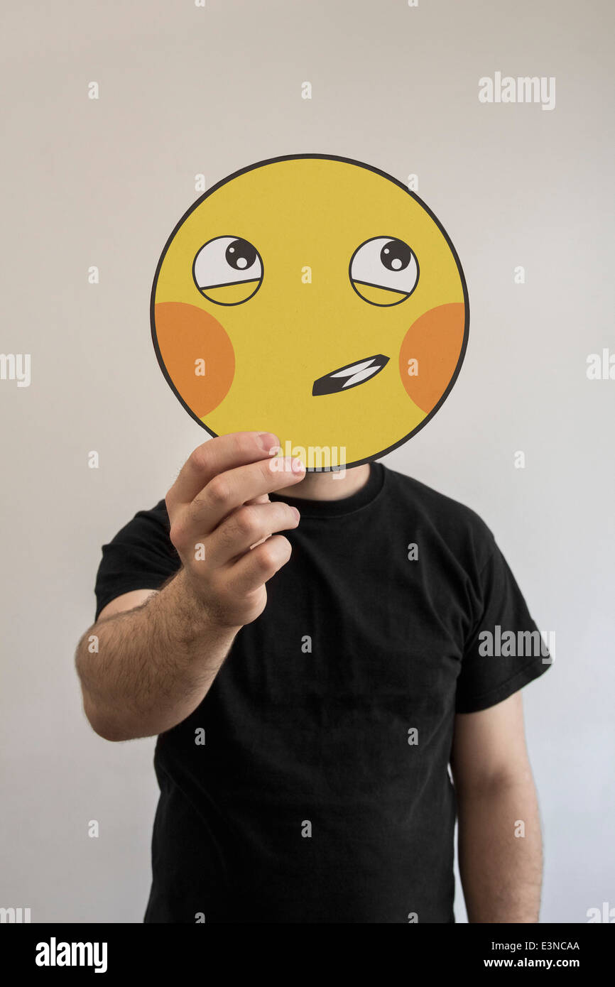Man holding a shy emoticon face in front of his face Stock Photo