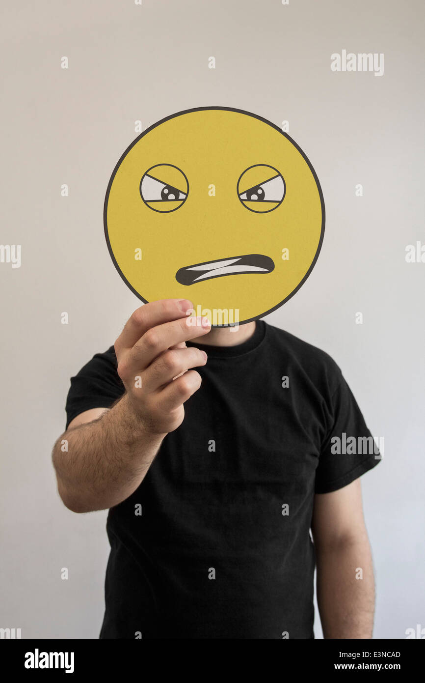 Man holding an angry emoticon face in front of his face Stock Photo