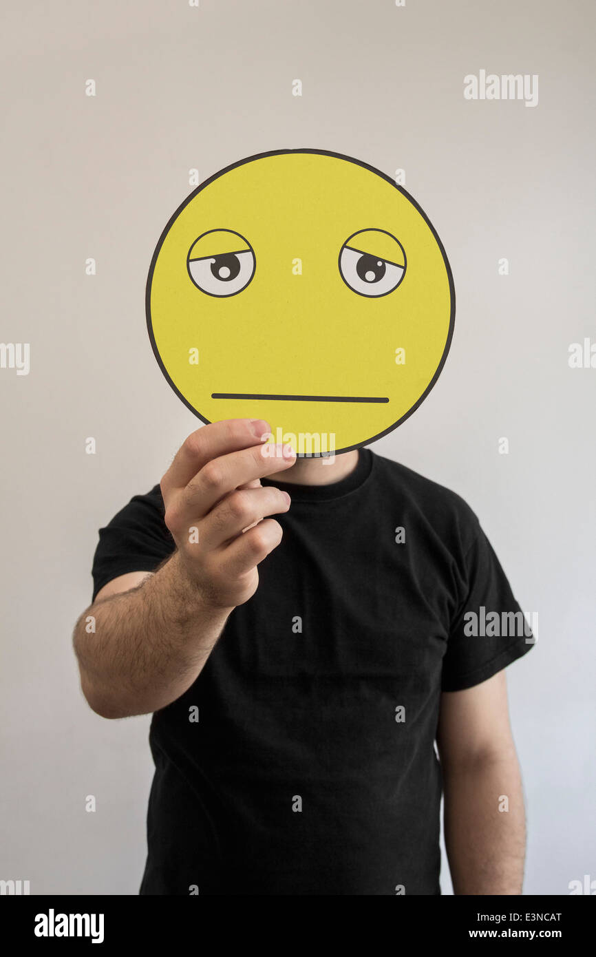 Man holding an exhausted emoticon face in front of his face Stock Photo