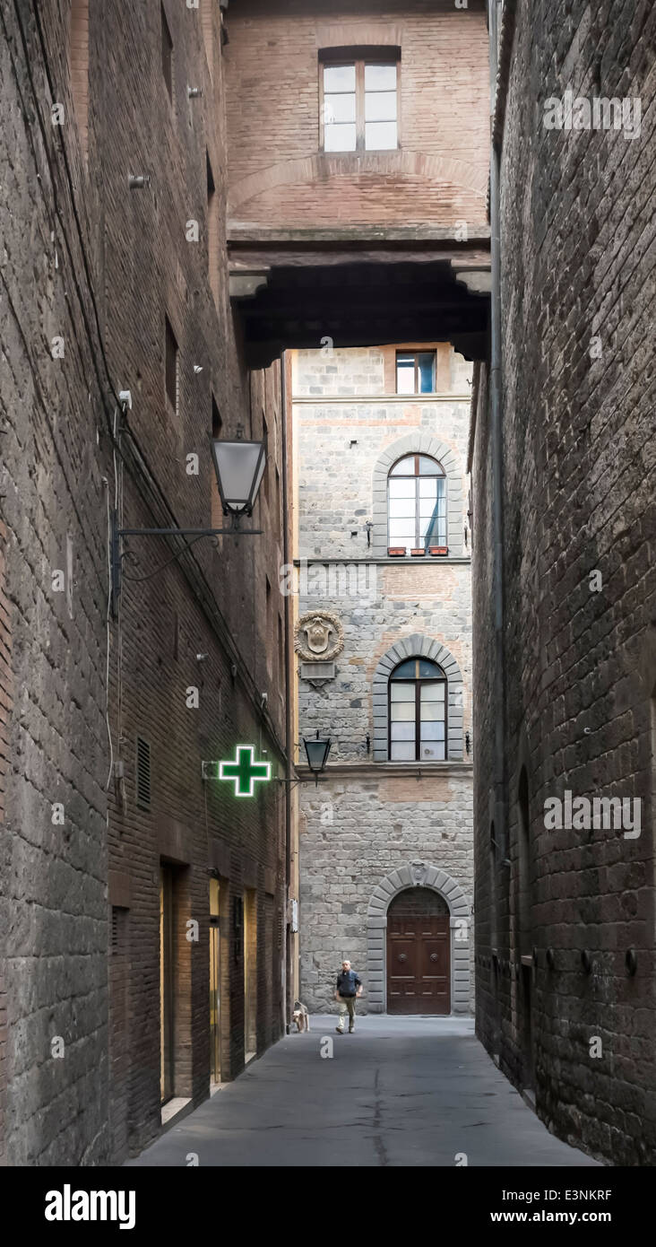 Man and dog in dark alley see the welcoming light of a pharmacy in the gloom: Siena, Tuscany, Italy Stock Photo