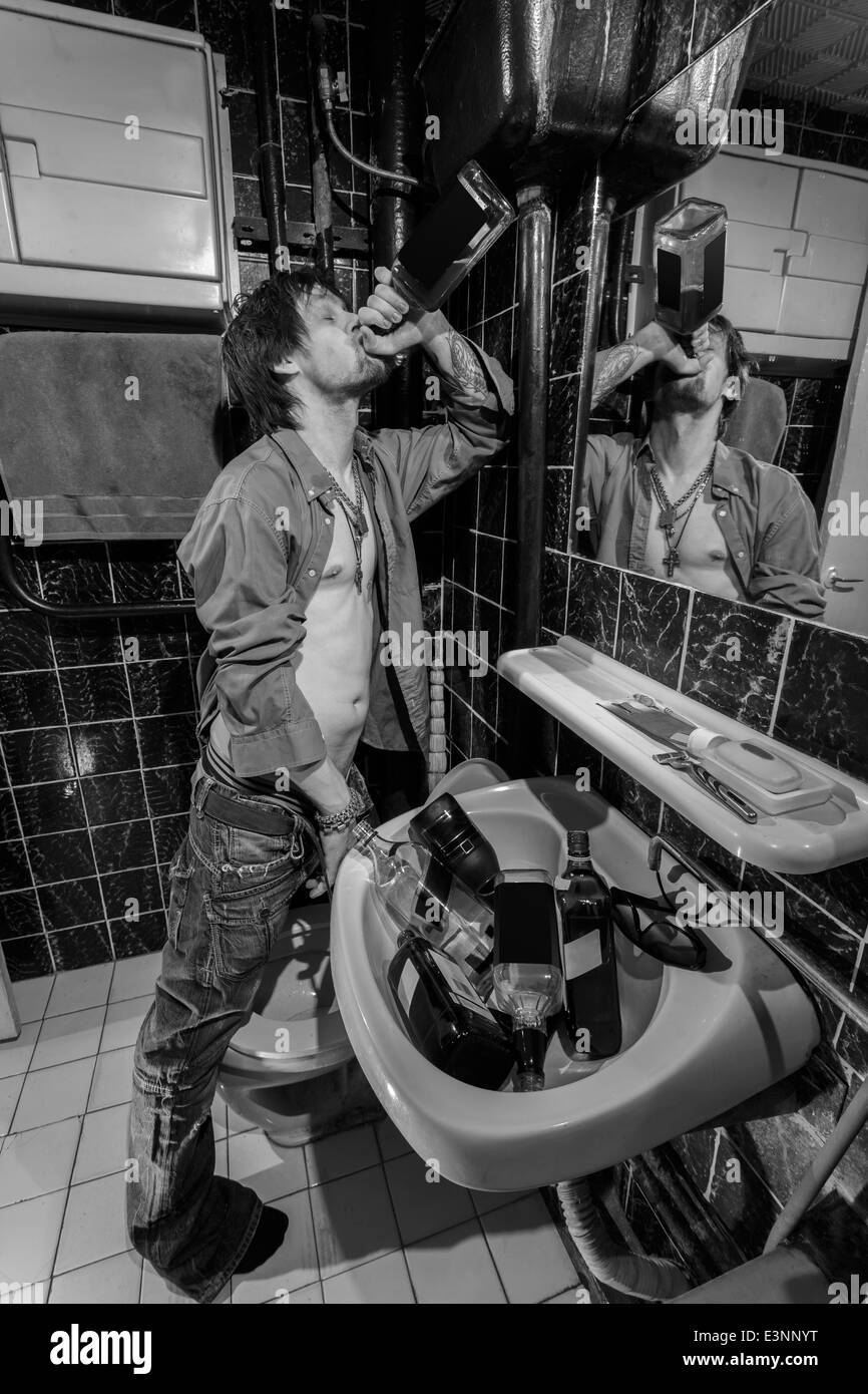 Drunk Man is standing in a toilet and drink whiskey. grayscale image Stock Photo