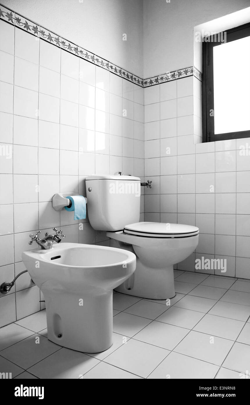 Black and white image of a restroom with toilet, bidet and blue toilet paper Stock Photo