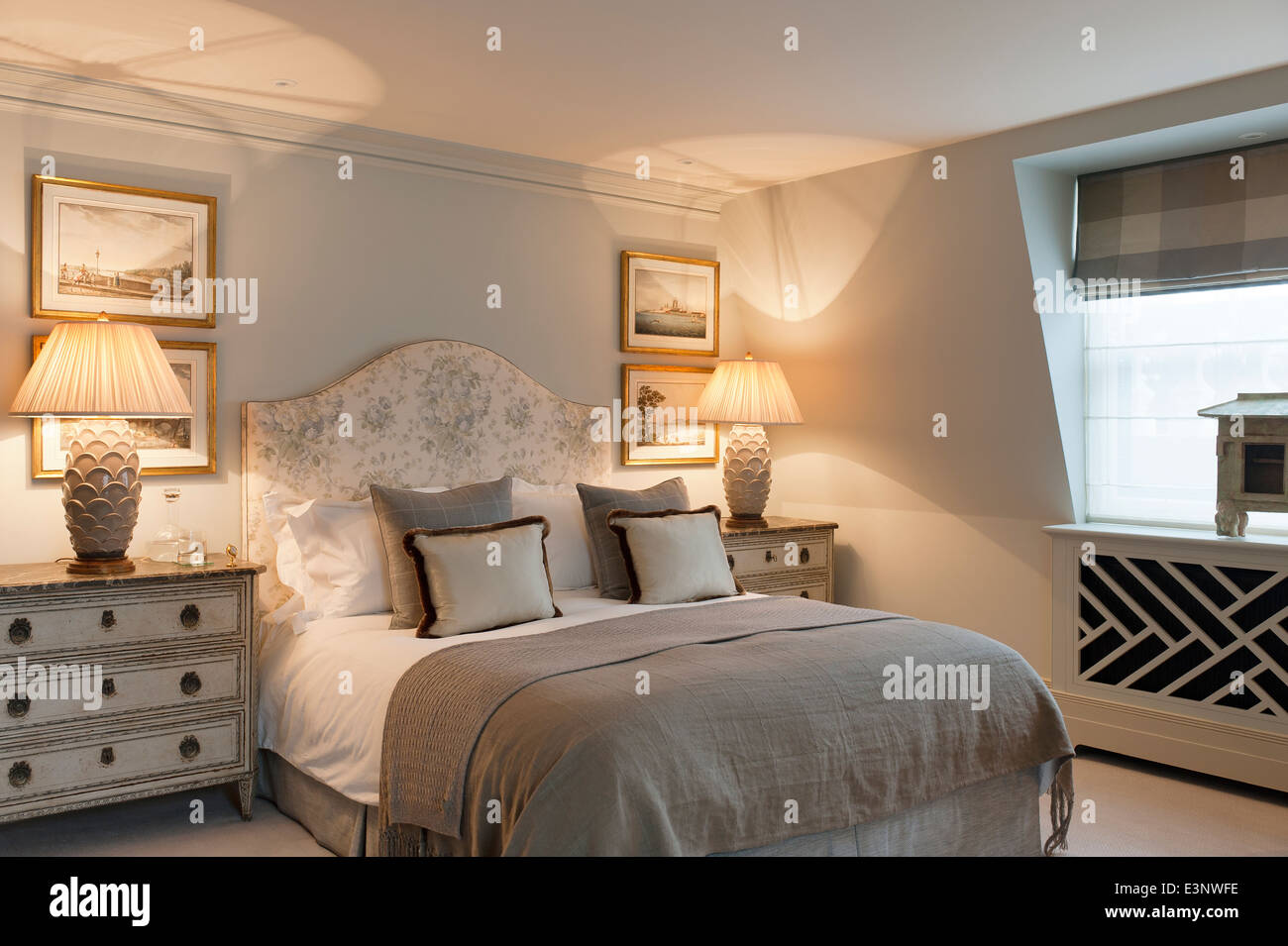 Elegant bedroom in earthy tones with floral patterned bed flanked by pair of wooden chests with lamps Stock Photo